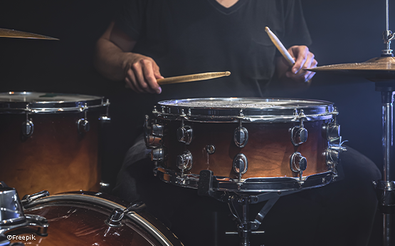 musicien en t-shirt noir joue de la batterie avec des baguettes sur scène