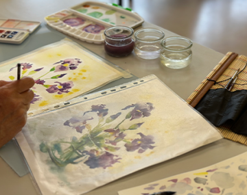 main femme qui peint avec de l'aquarelle une fleur polyèdre seynod annecy